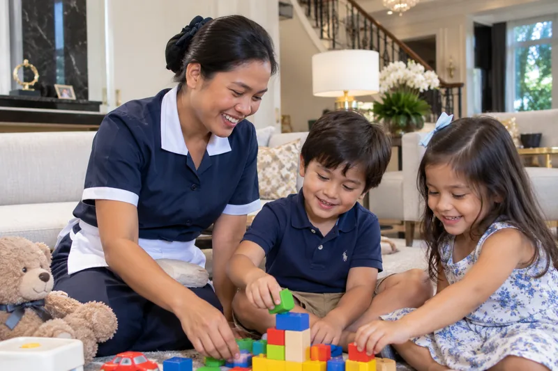 Filipino domestic helper in uniform smiling and building with toy blocks together with two young children in a family living room